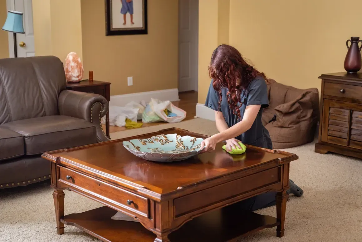 A woman is cleaning a coffee table in a living room.