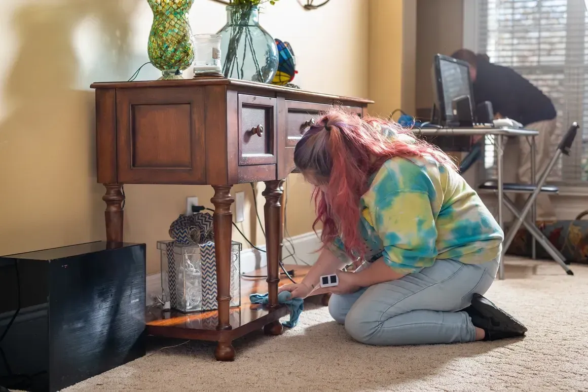 A woman is kneeling down in front of a wooden table in a living room.