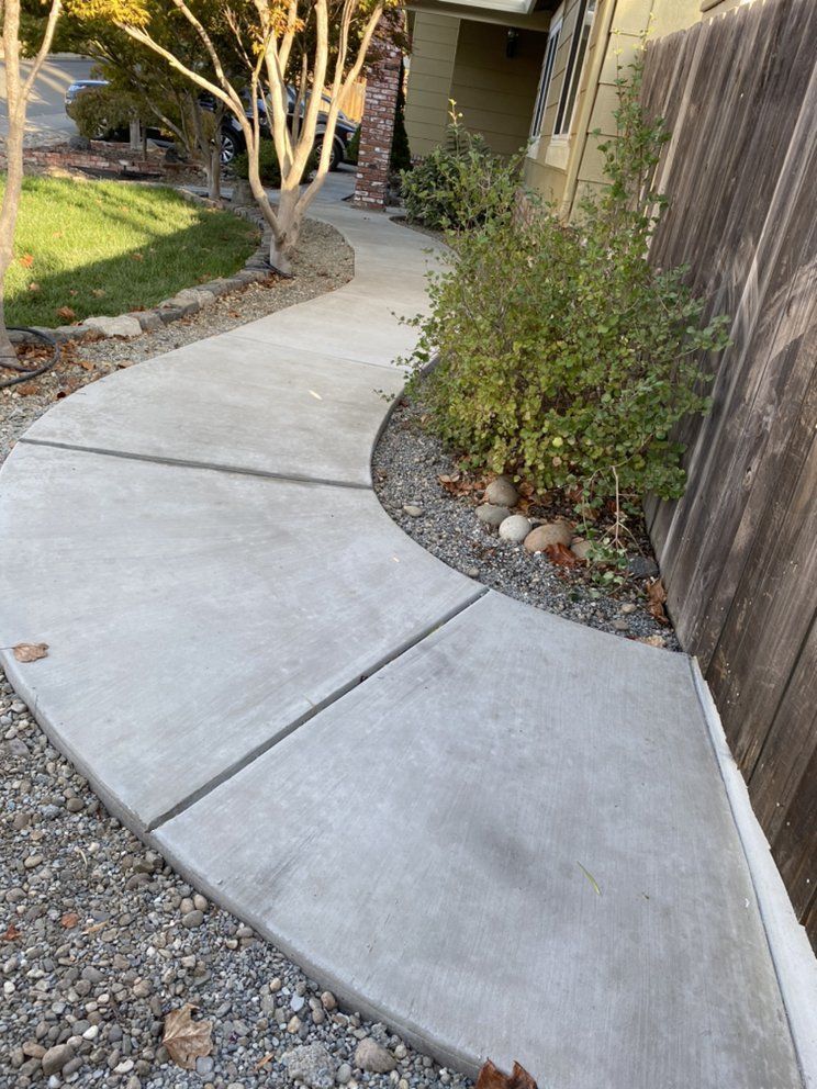 A concrete walkway leading to a house with a wooden fence.