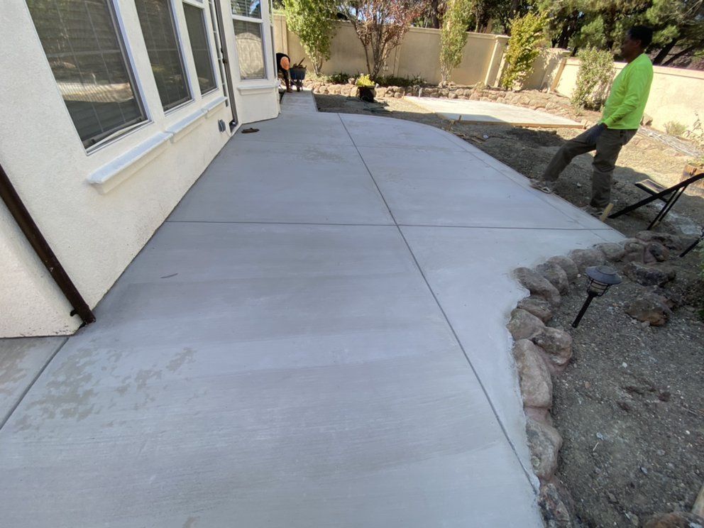 A man is standing on a concrete sidewalk in front of a house.