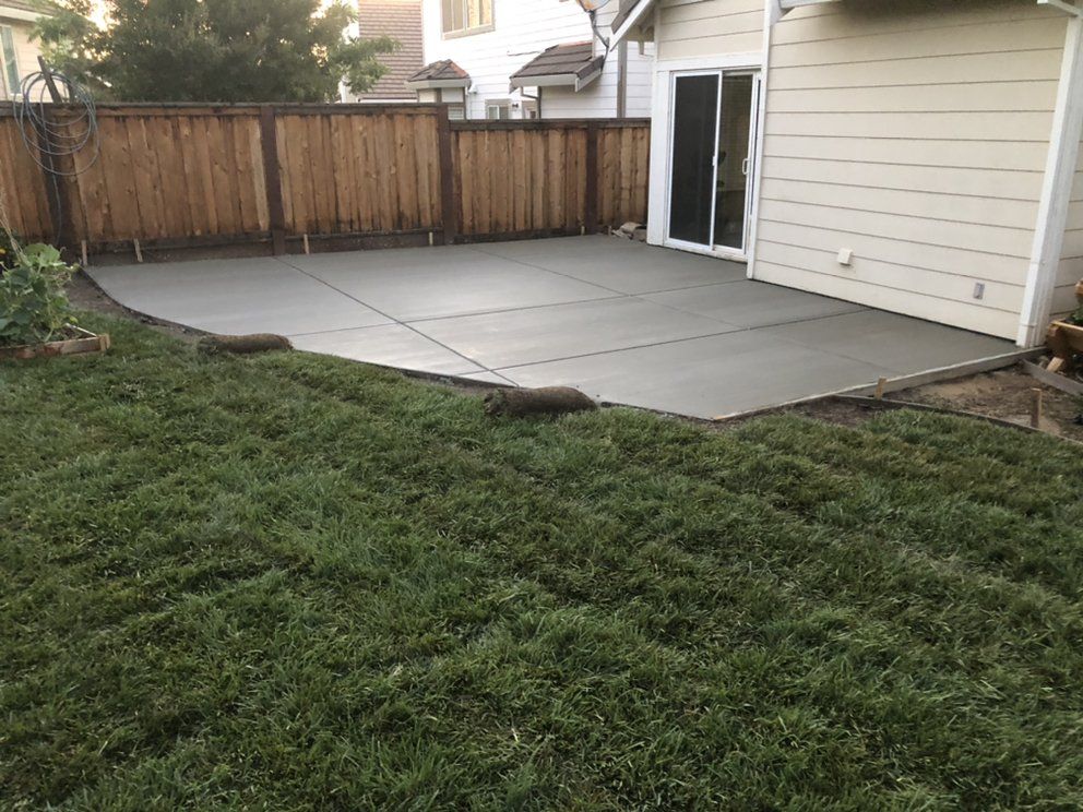 A backyard with a concrete patio and a wooden fence.