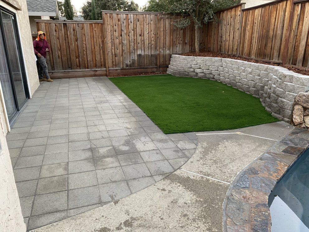 A man is standing in the backyard of a house with a fence and a patio.
