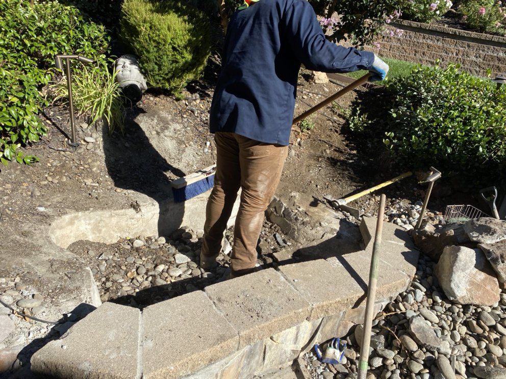 A man in a blue shirt is raking rocks in a garden
