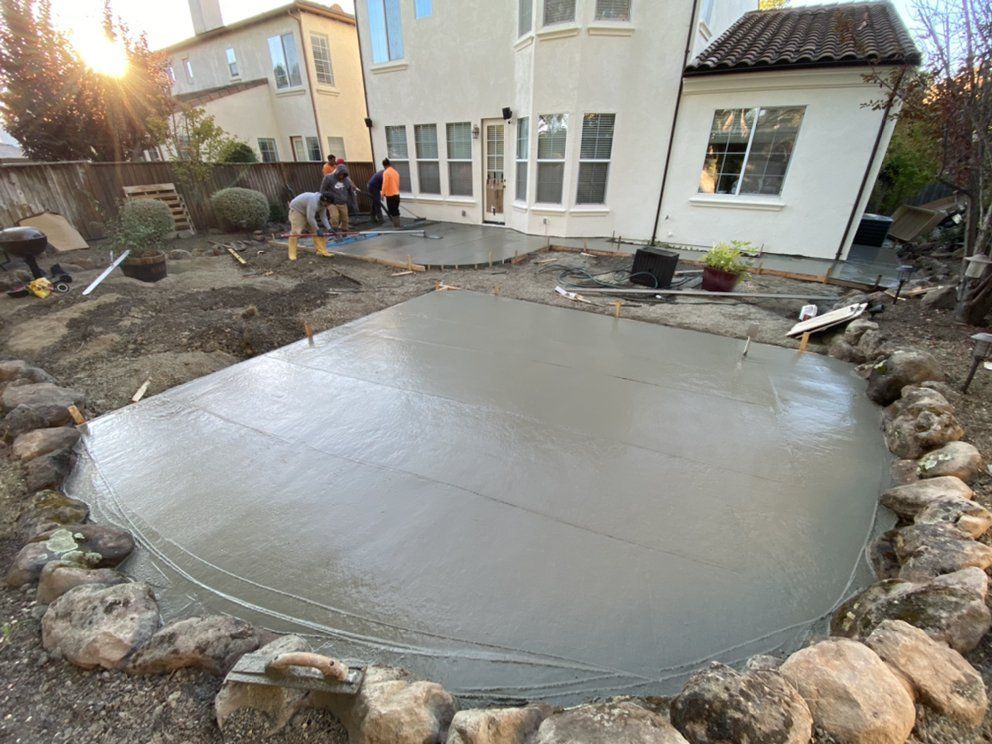 A group of people are working on a concrete patio in front of a house.