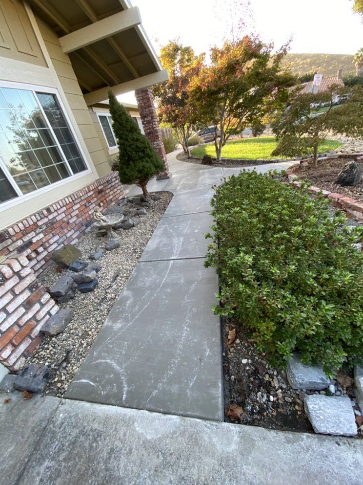 A concrete walkway leading to a house with a brick wall.