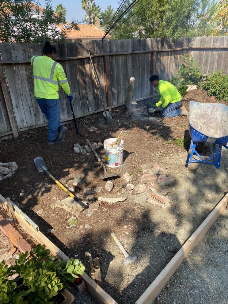 Two men are working in a backyard with shovels and a wheelbarrow.