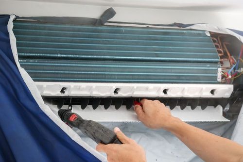 A technician uses a pressure washer tool to clean the interior coils and blower wheel of a wall-mounted air conditioner.