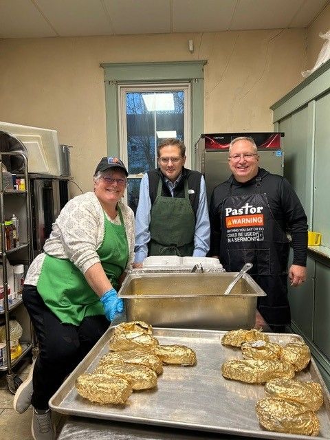 Three people in a kitchen prepare food. One wears a 