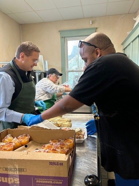 Three people in a kitchen preparing food, one person is putting food into containers.