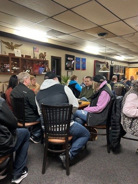 People seated at tables in a dimly lit room, possibly a bar or community center.