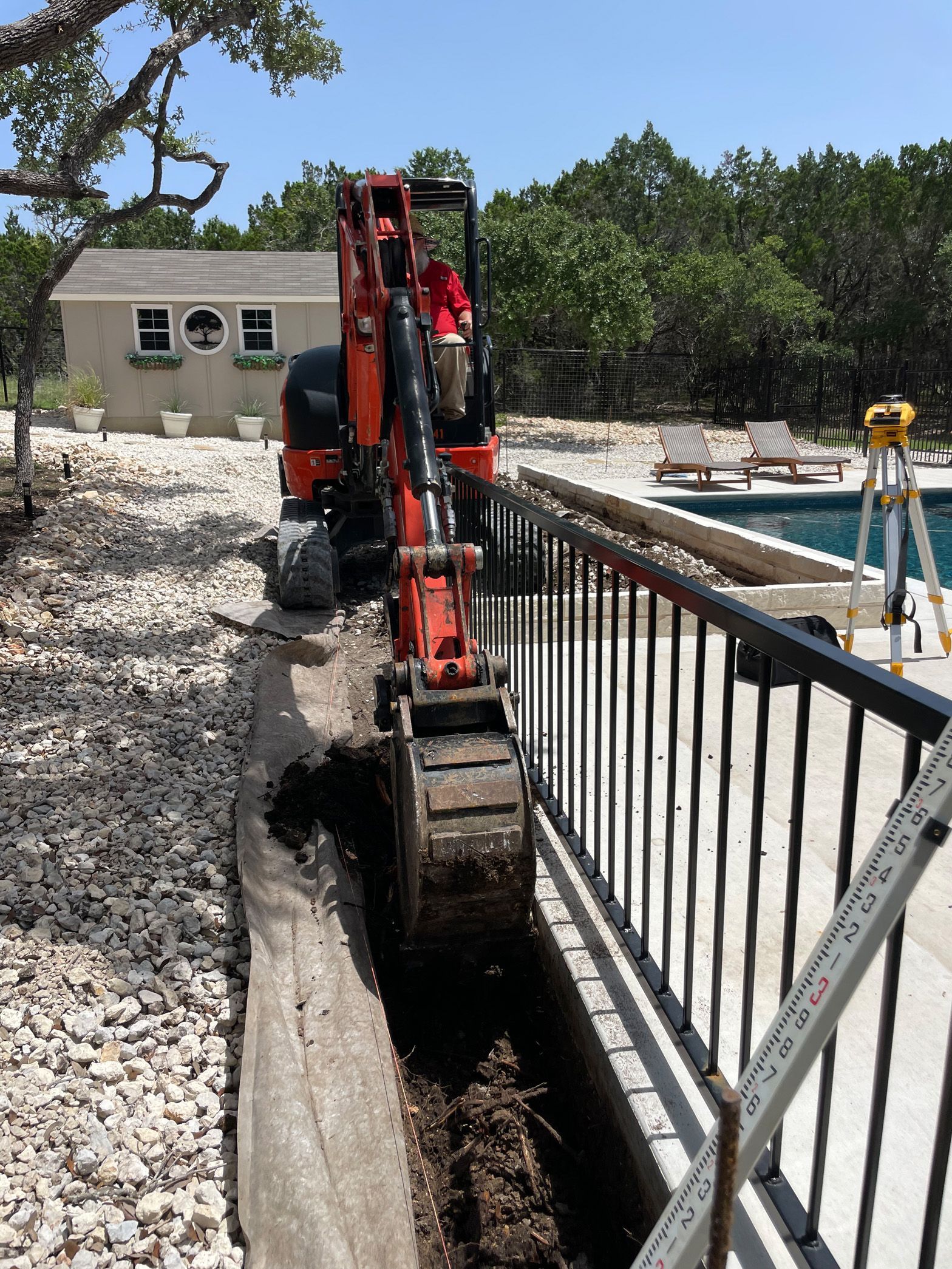 An excavator is digging a hole in the ground next to a pool.