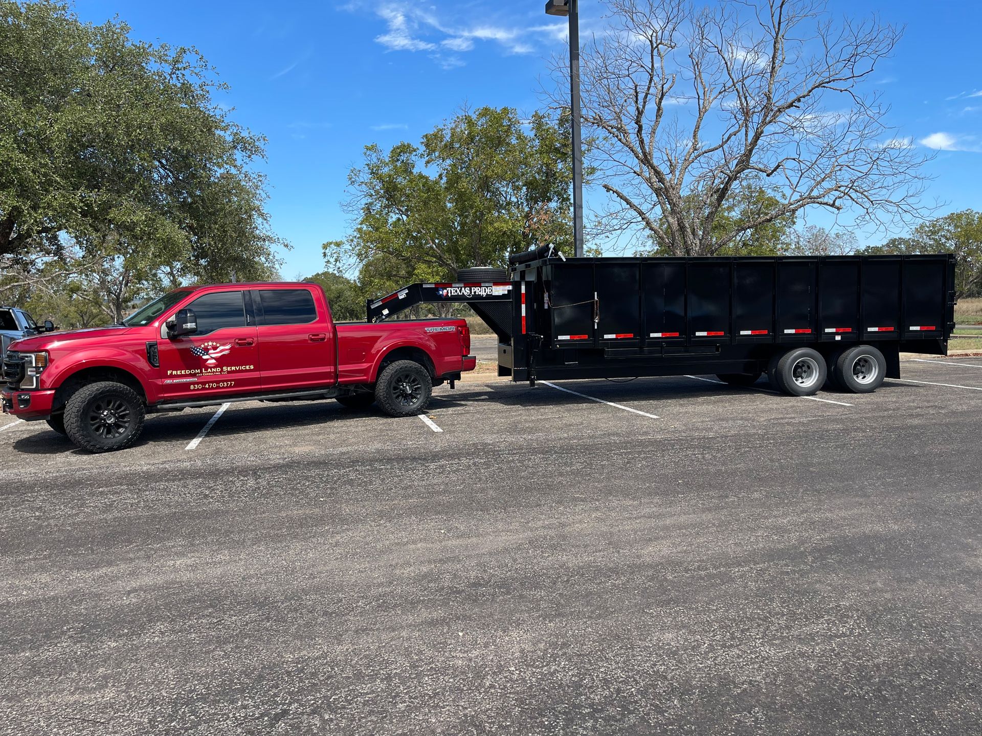 A red truck is towing a dump trailer in a parking lot.