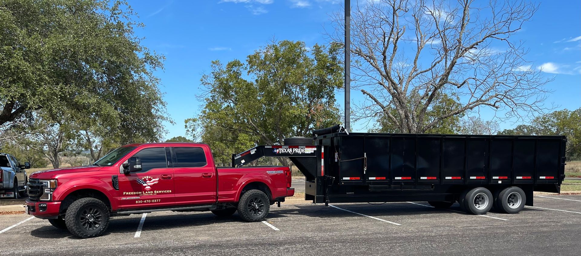 A red truck is towing a dump trailer in a parking lot.