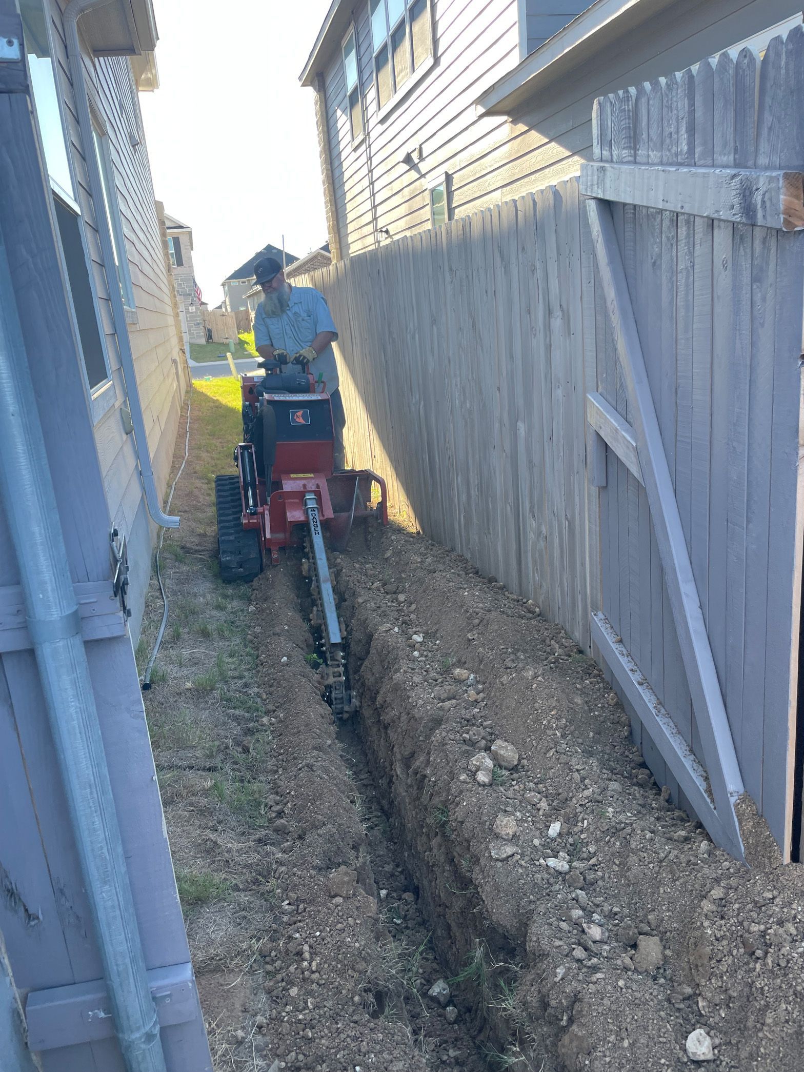 A man is using a machine to dig a trench in the side of a house.