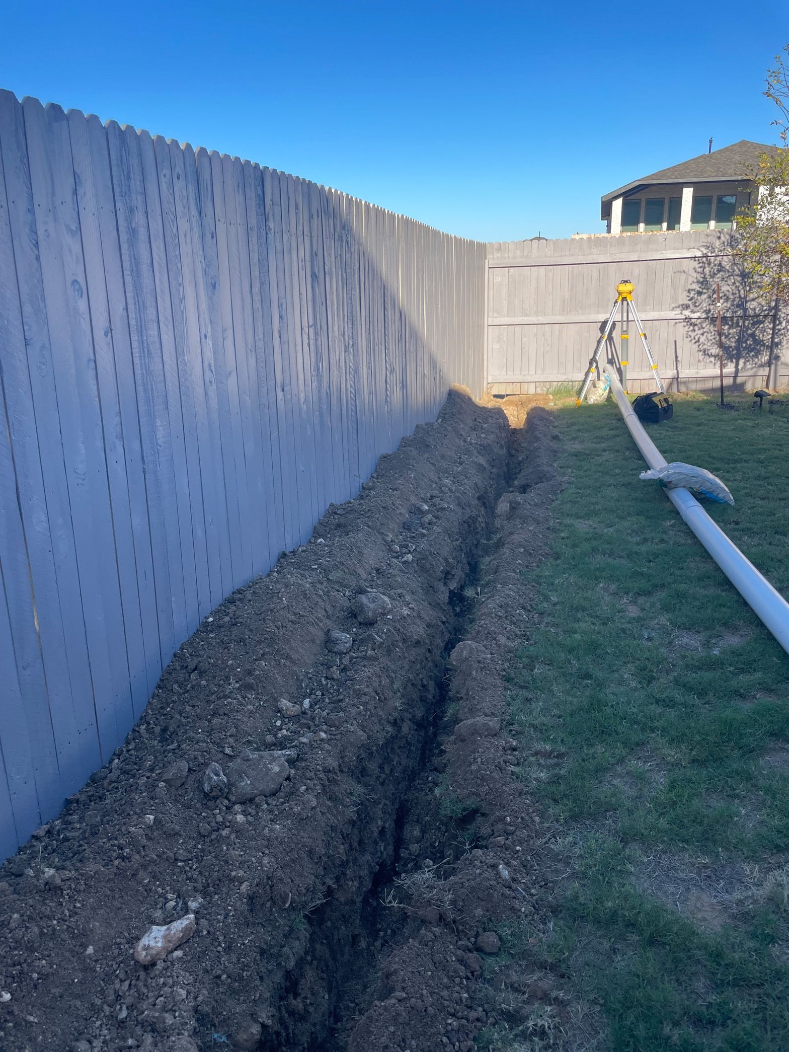 A hose is laying in the dirt next to a fence.