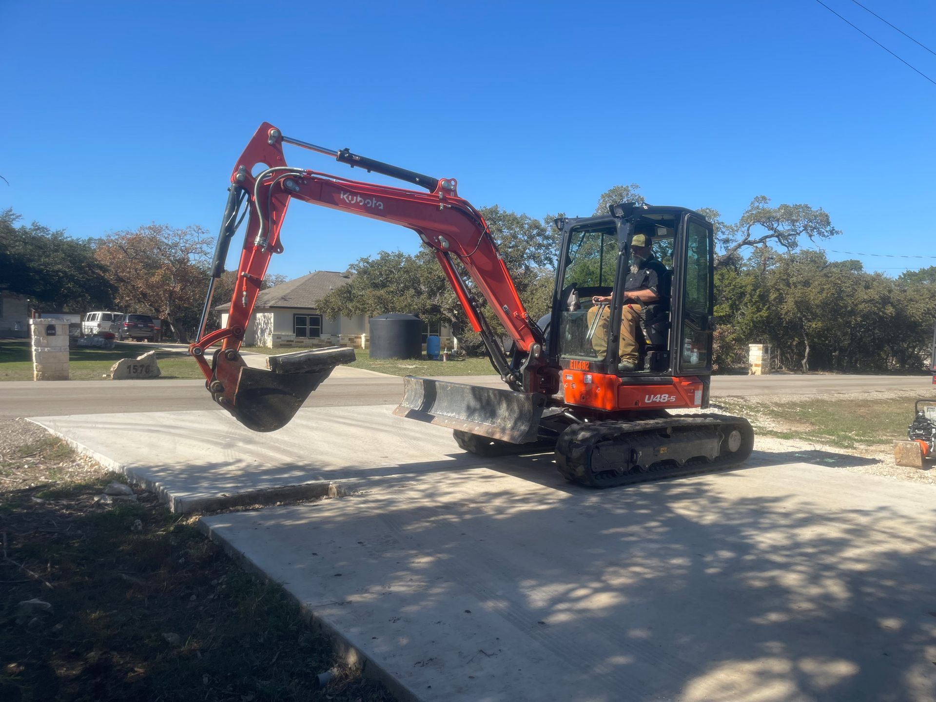 A red excavator is parked in a driveway next to a house.