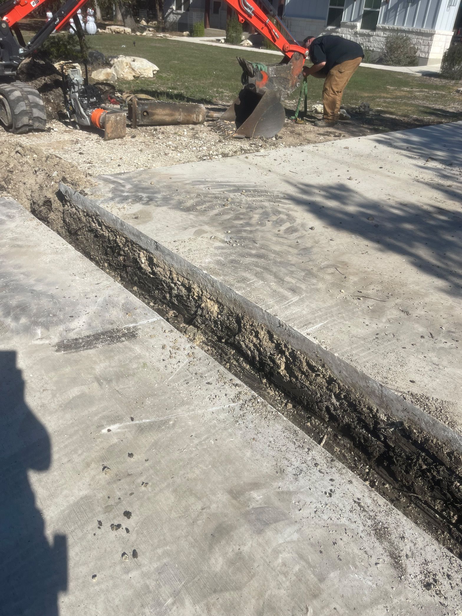 A man is working on a concrete driveway with an excavator.