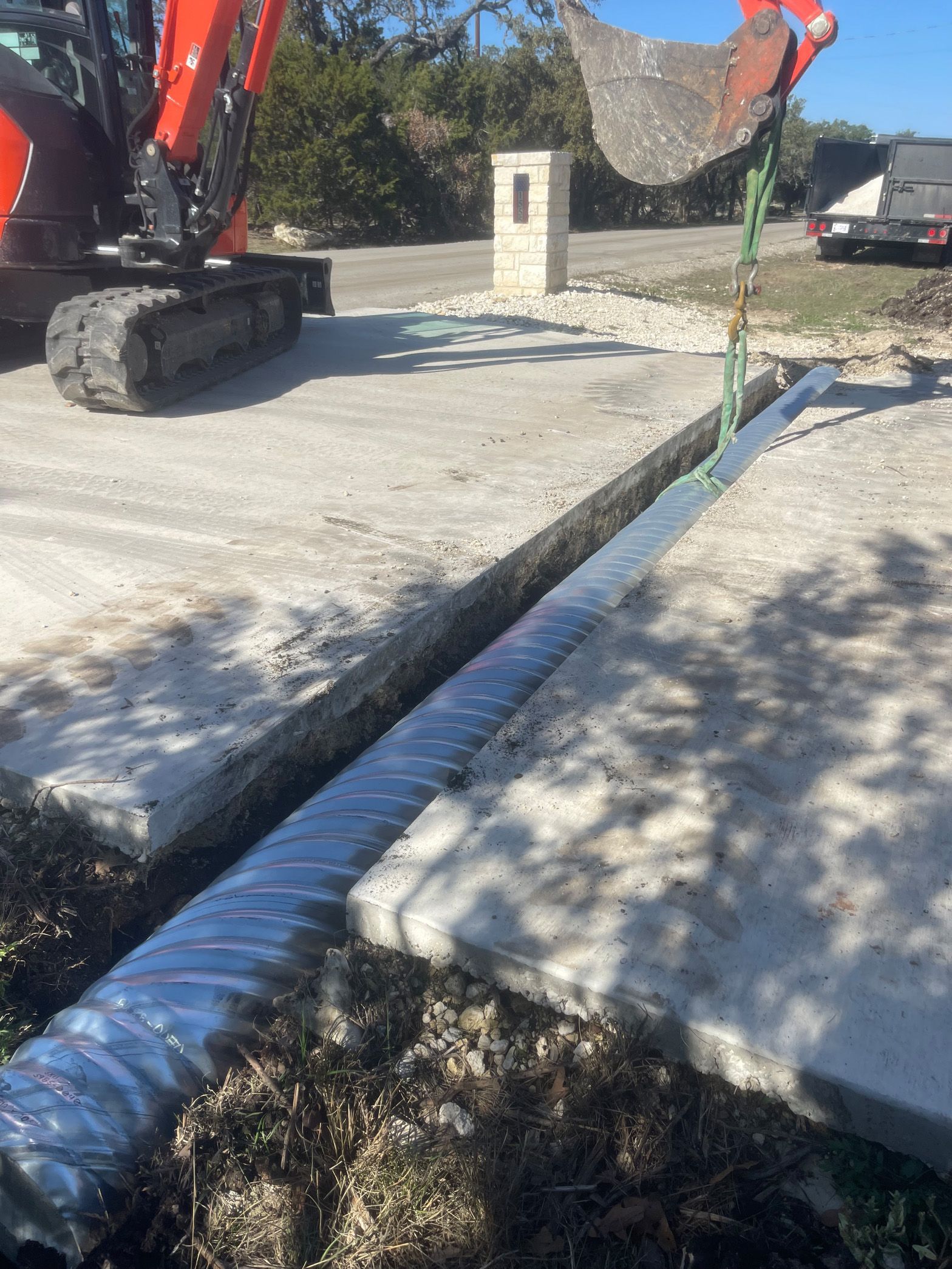 An excavator is digging a hole in the ground next to a sidewalk.