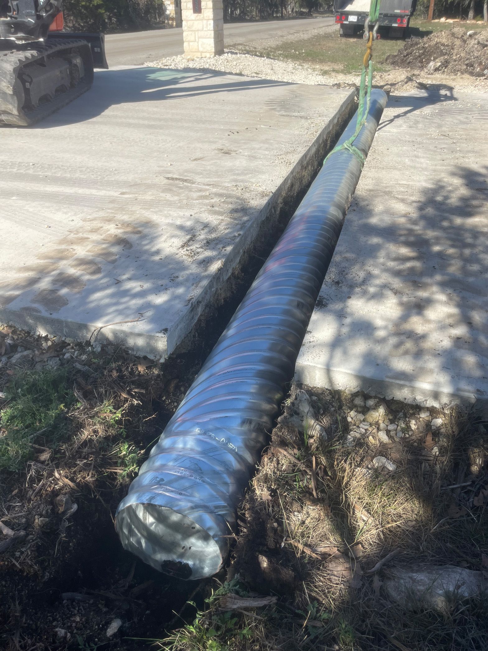 A large pipe is sitting in the dirt next to a concrete curb.