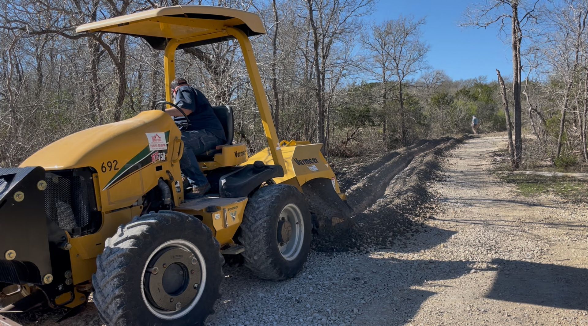 A man is driving a yellow tractor on a dirt road.