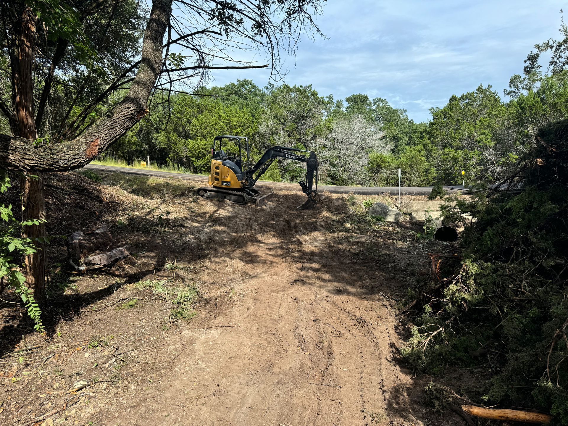 A small excavator is working on a dirt road in the woods.