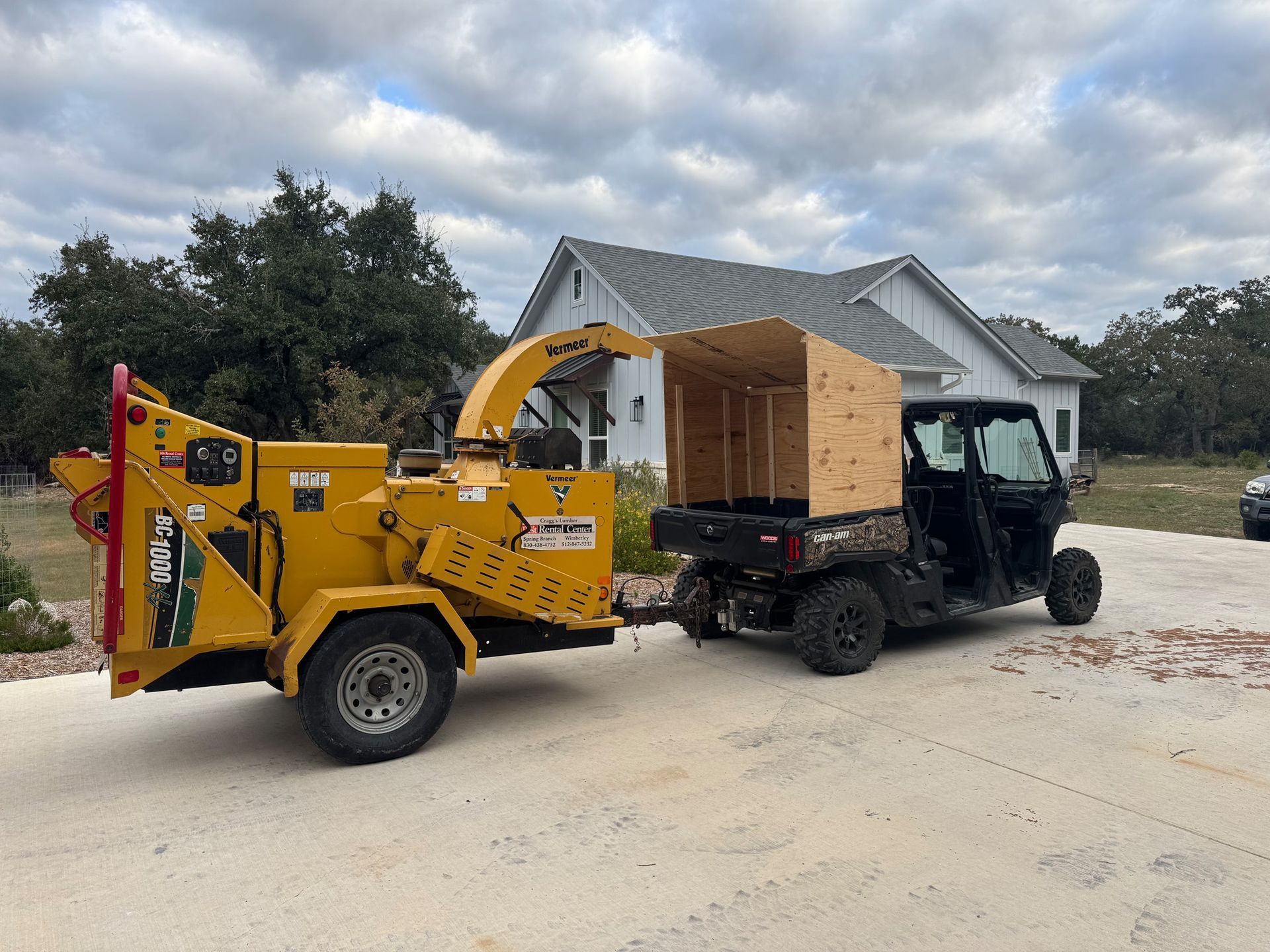 A wood chipper is being towed by a utility vehicle in front of a house.