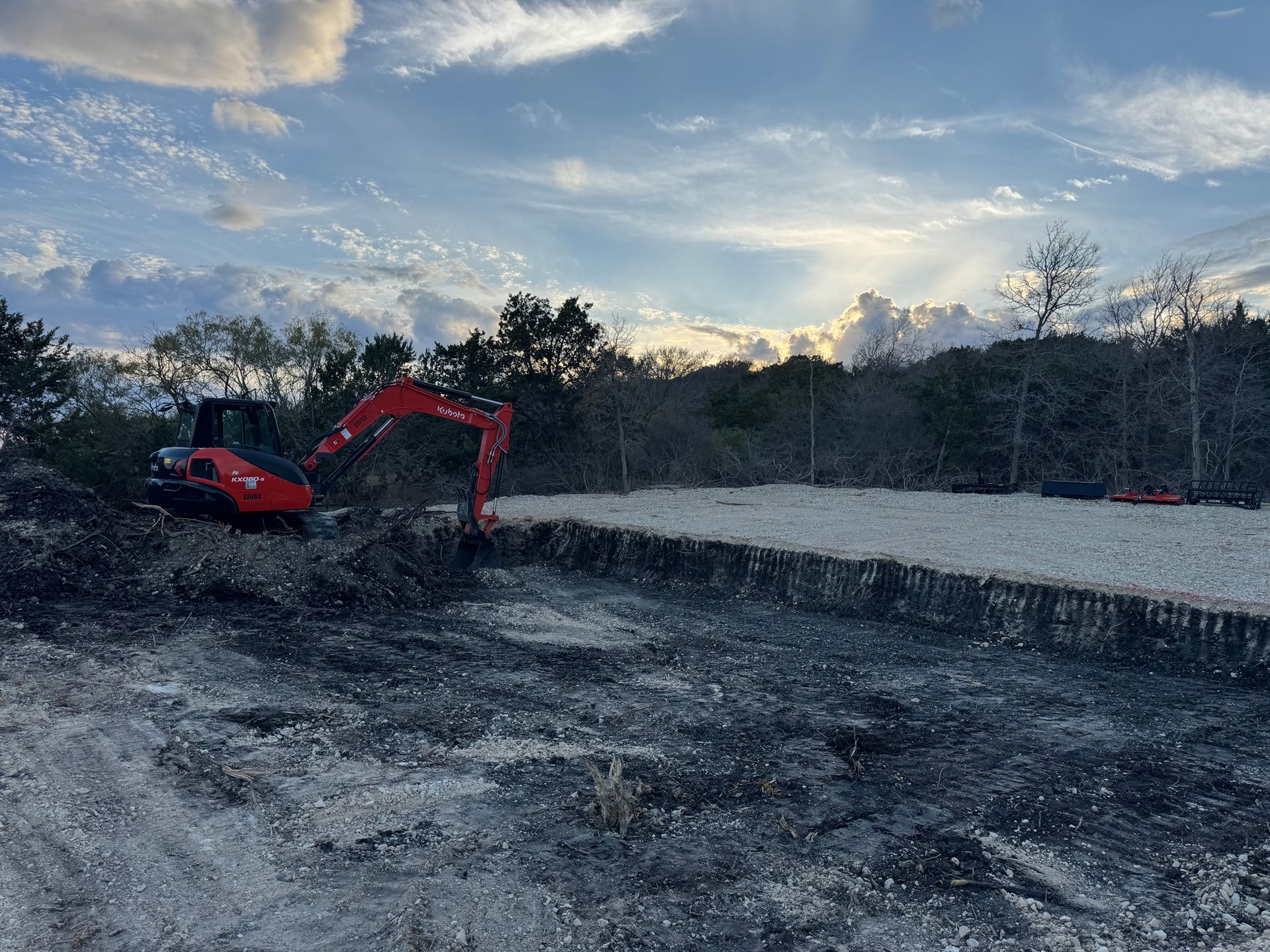 A red excavator is digging a hole in the dirt in a field.