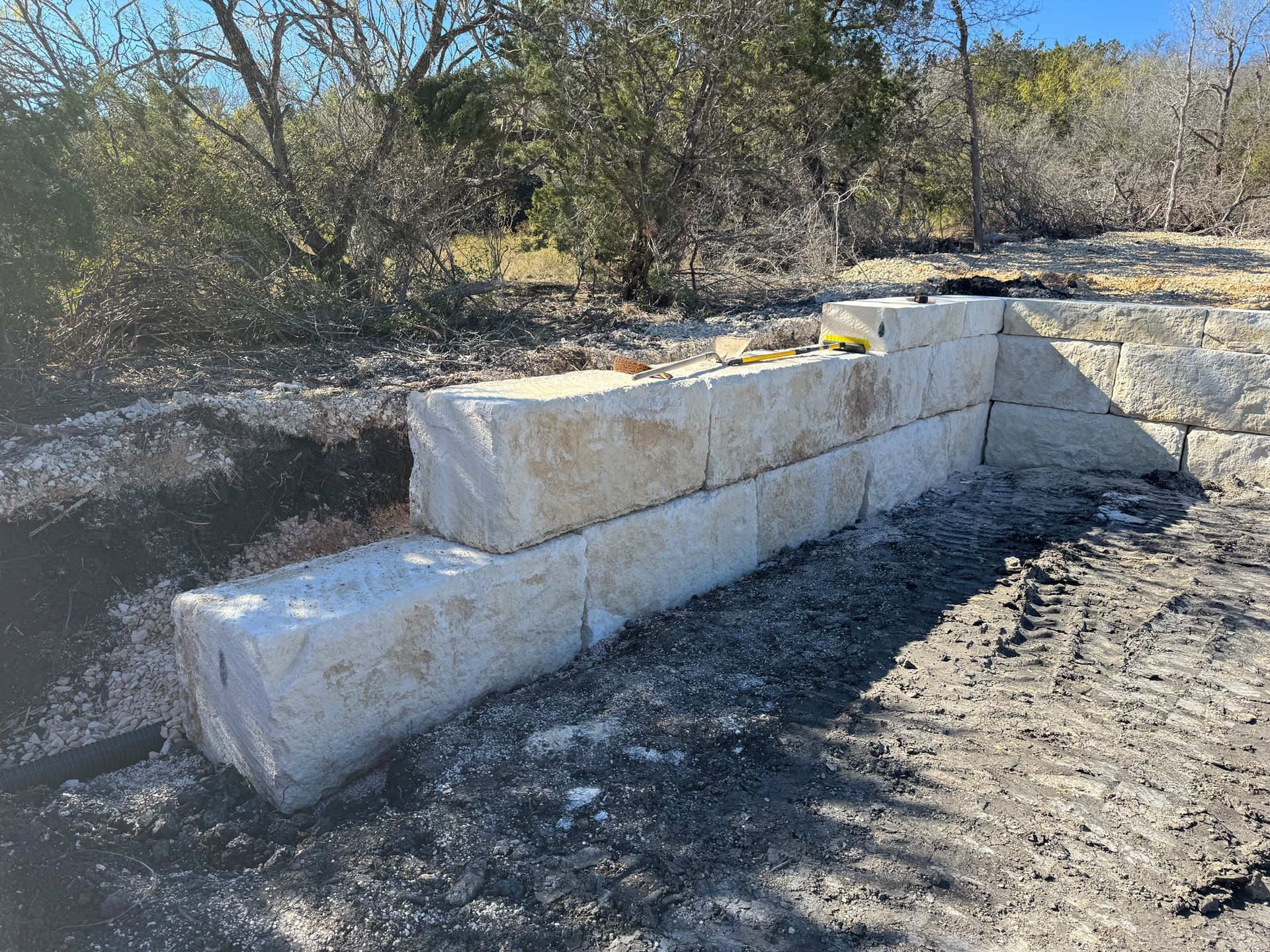 A stone wall is being built in the dirt in the middle of a forest.