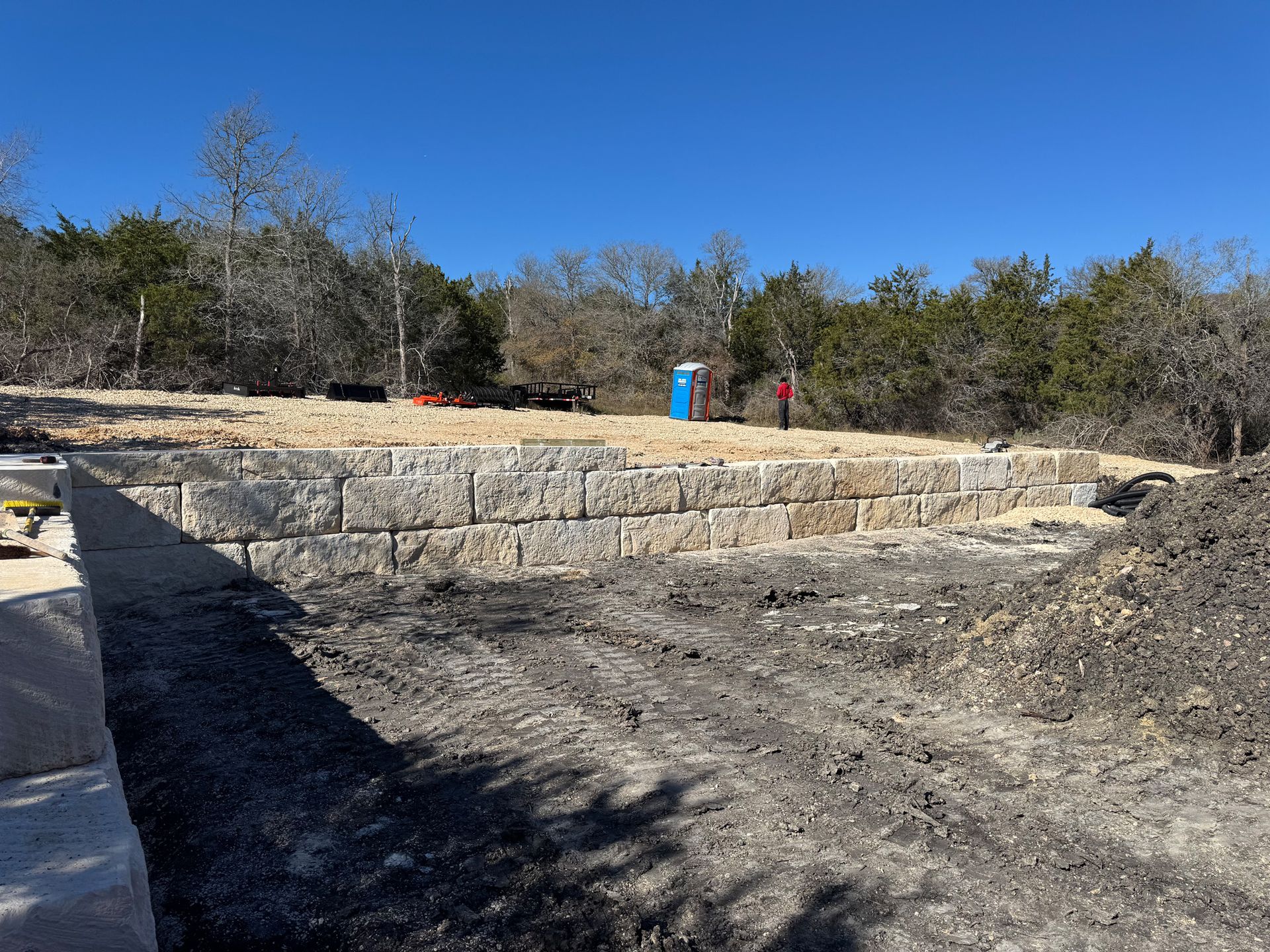 A large pile of dirt is sitting on top of a dirt field next to a stone wall.