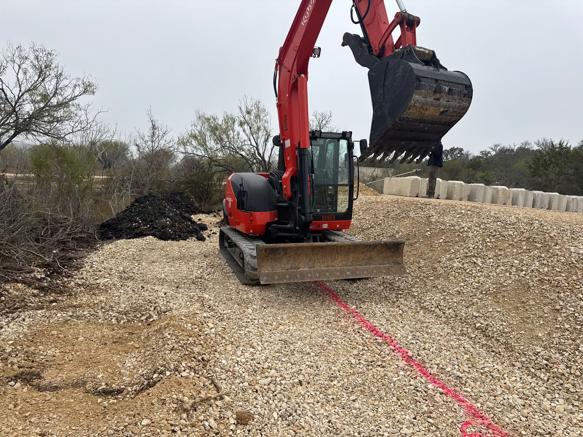 A red excavator is sitting on top of a pile of gravel.