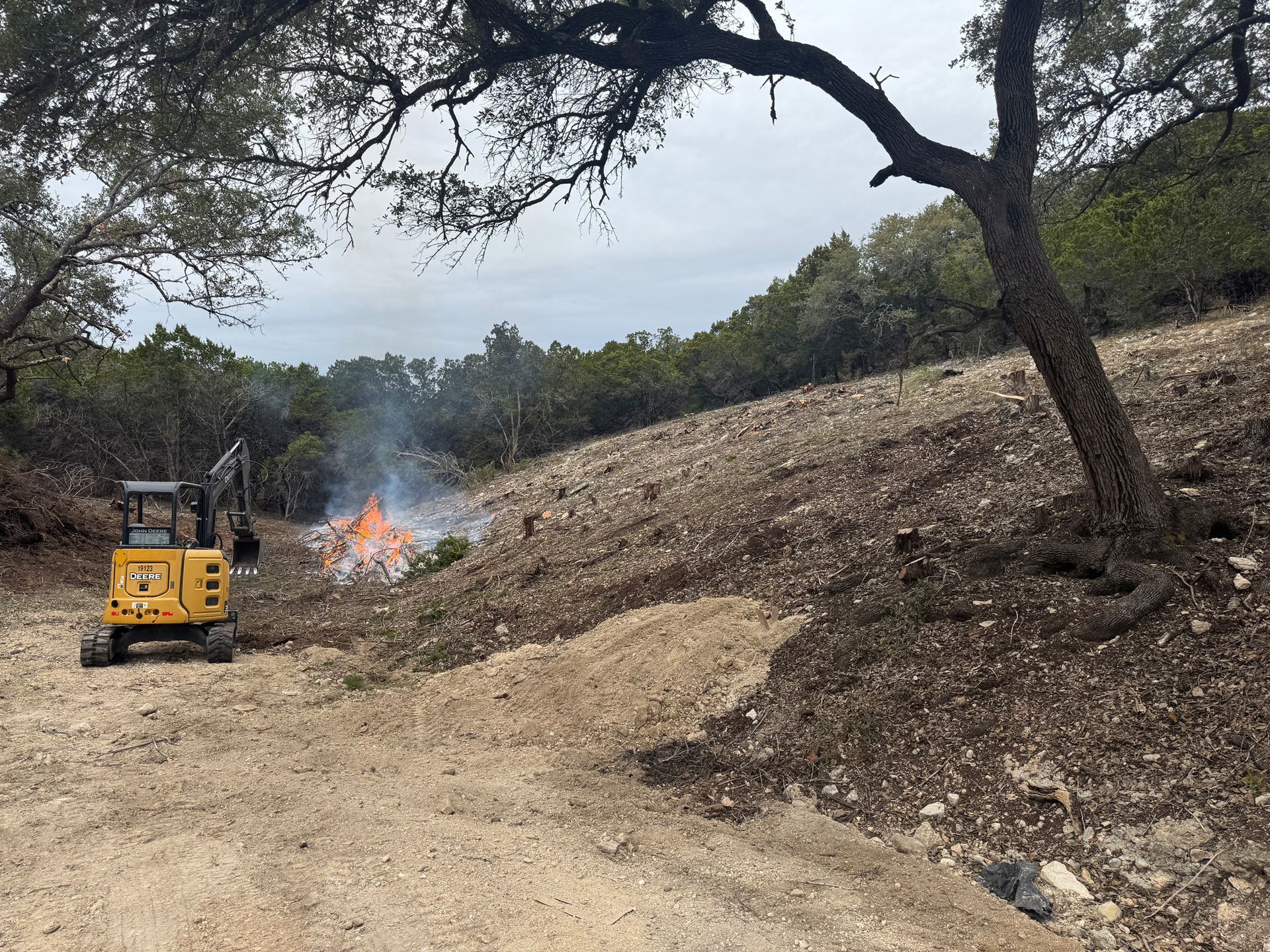 A bulldozer is driving down a dirt road next to a fire.