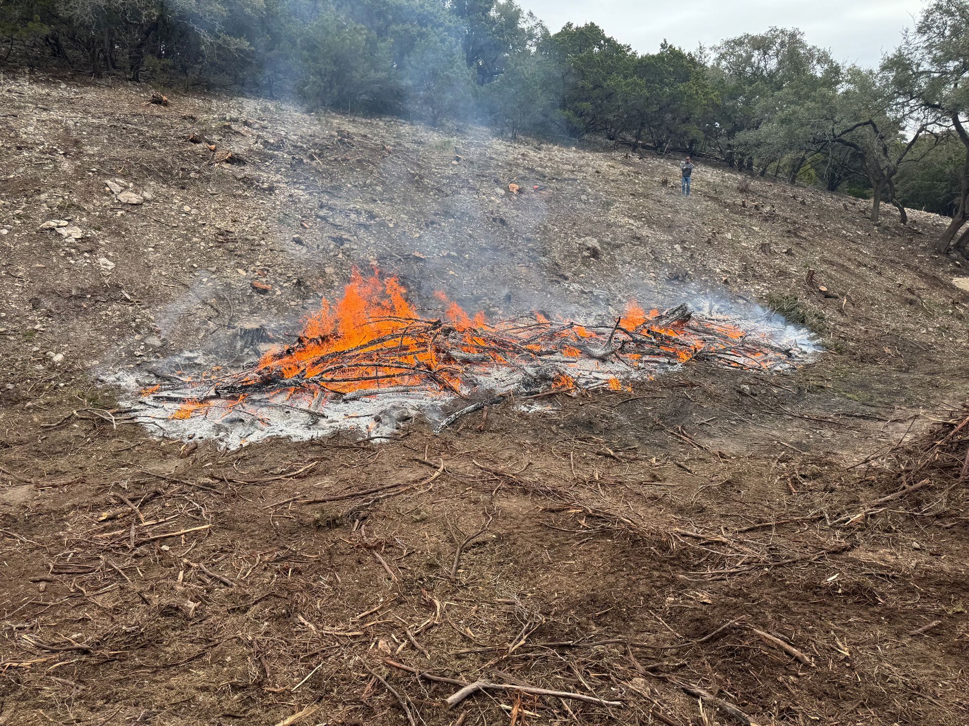 Burning pile of brush on a brown hillside, with flames and smoke.