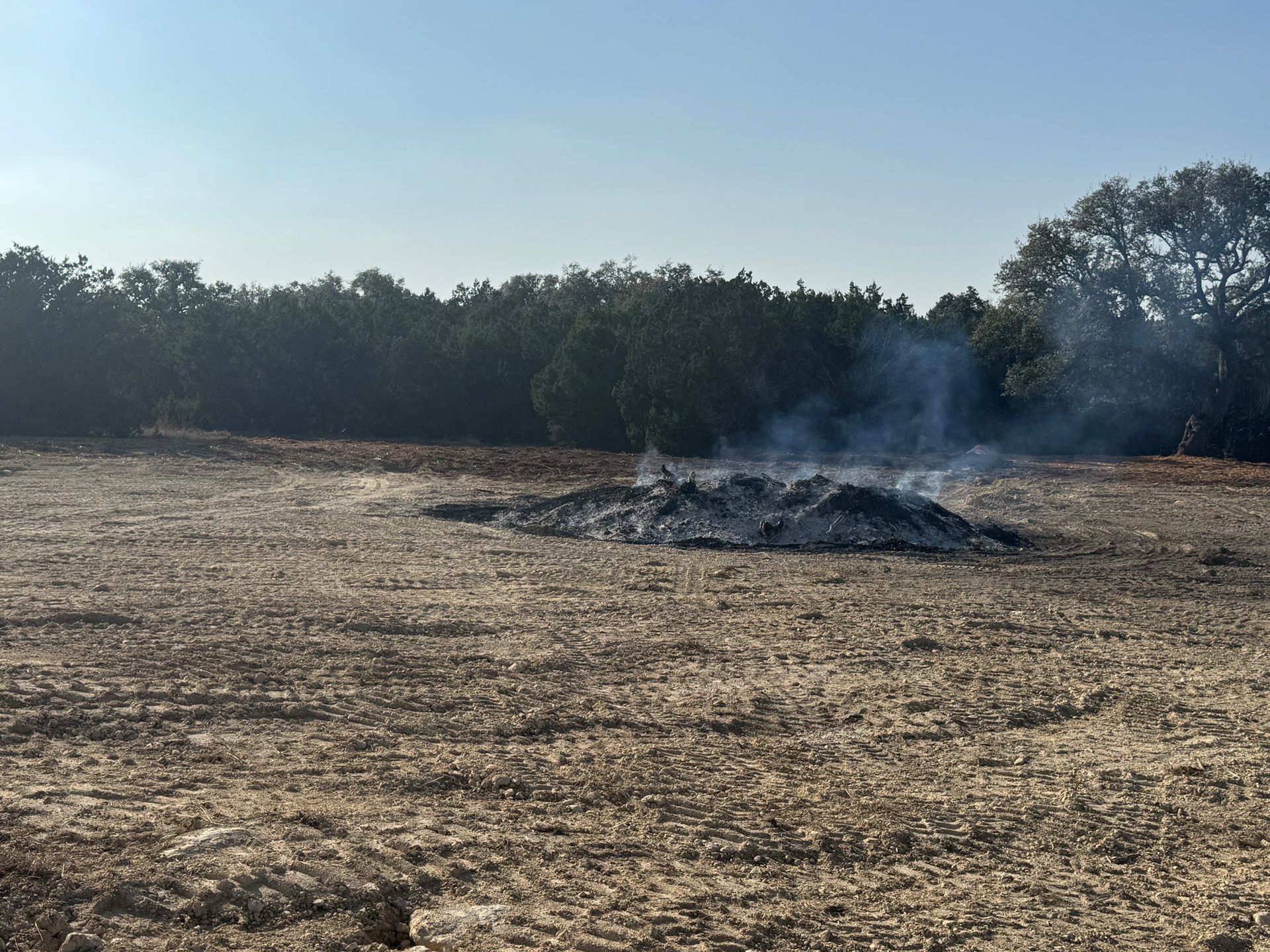 A field with smoke coming out of it and trees in the background.