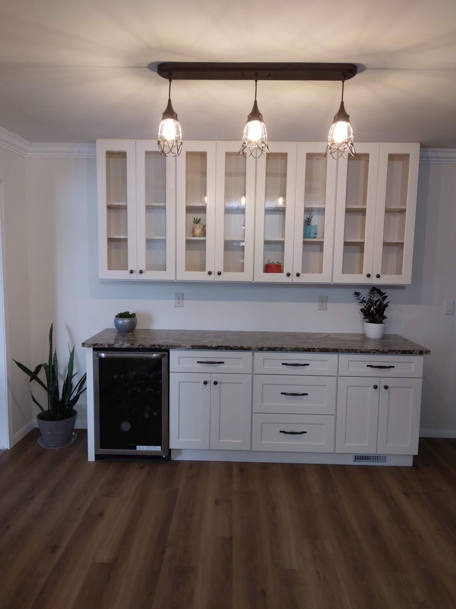 White cabinets with countertops, wine fridge, and overhead lighting in a bar area.