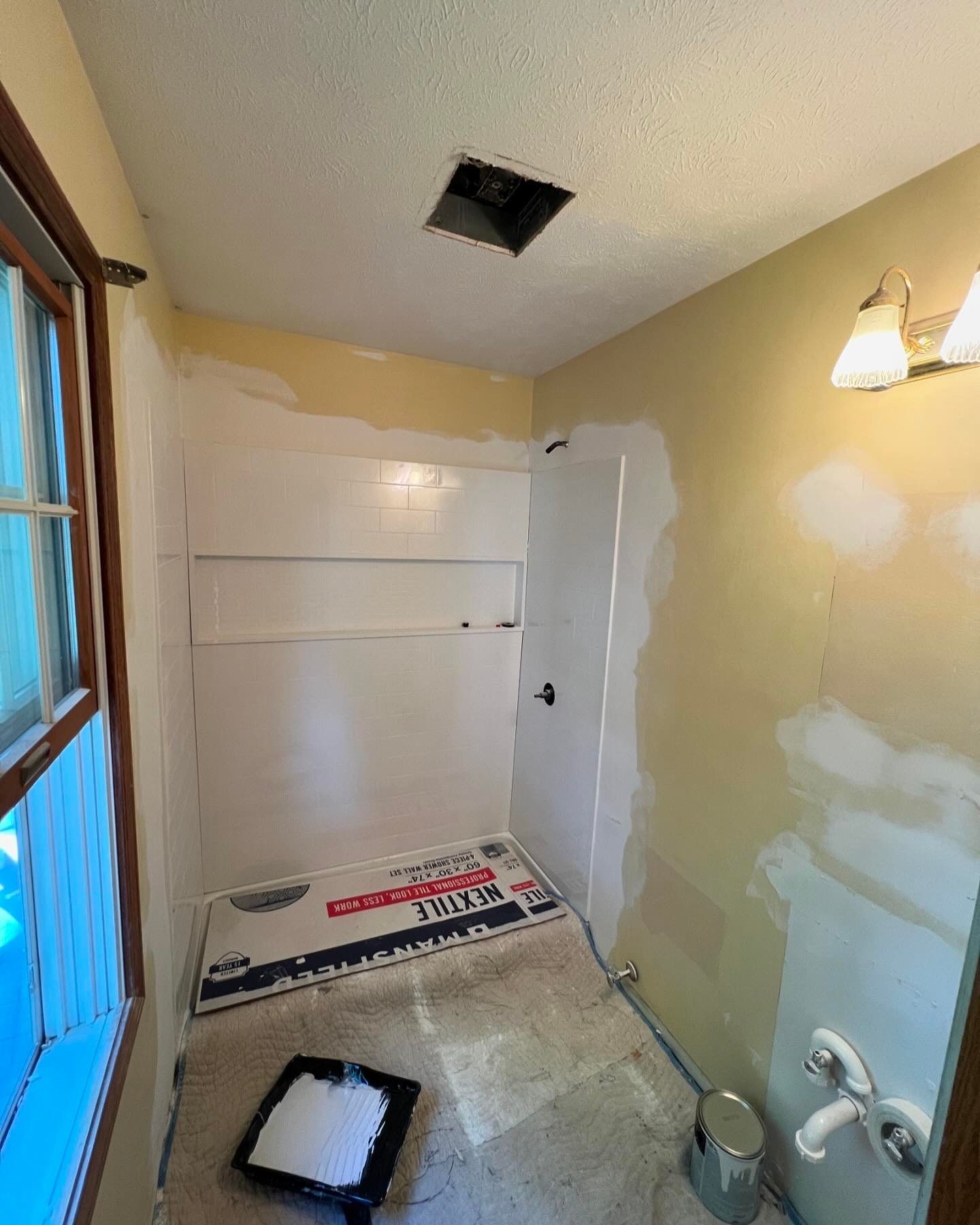 Bathroom renovation in progress; white shower, partially painted walls, paint tray on the floor.