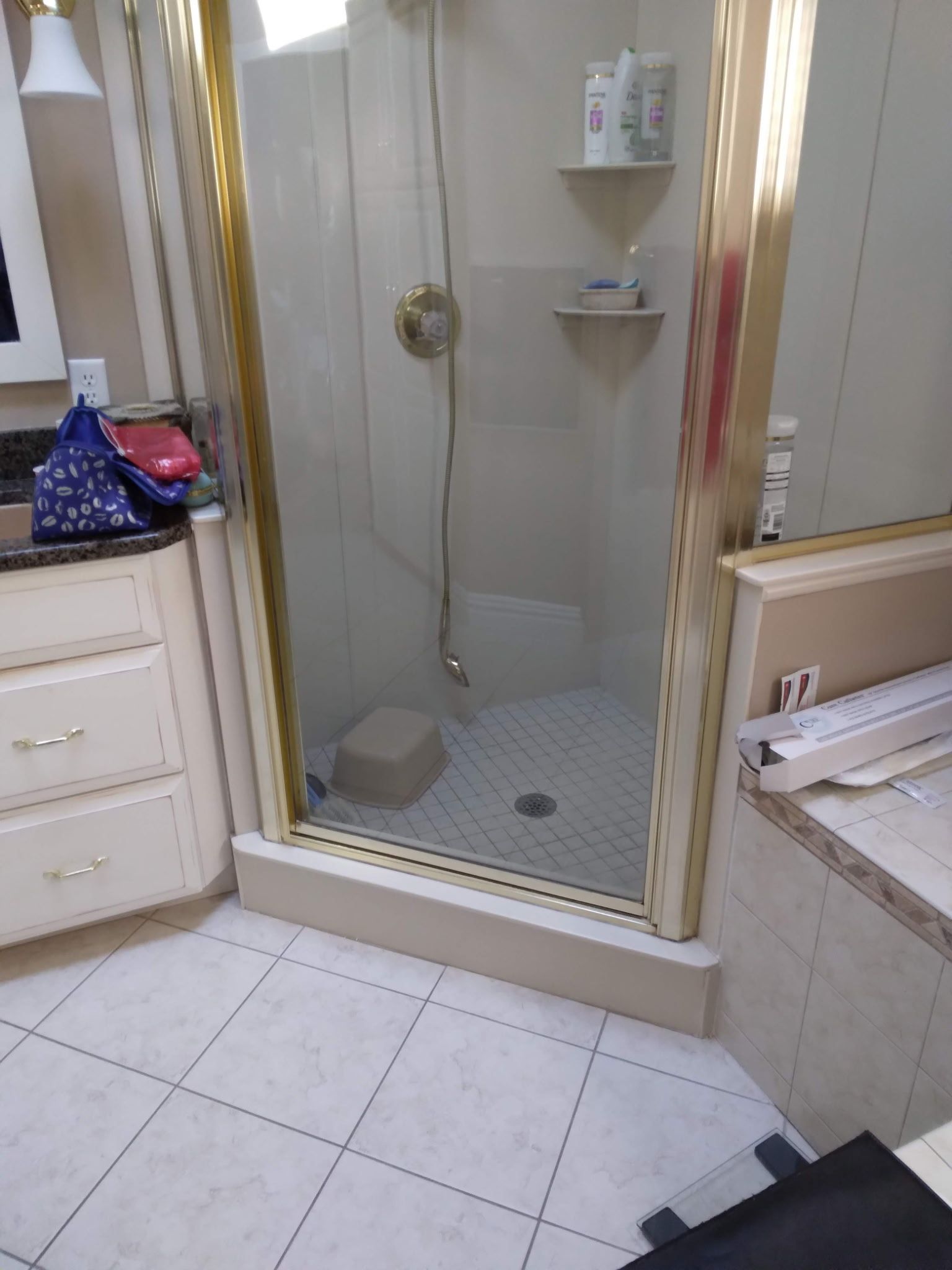 Bathroom with shower, vanity, and beige tile floor. Shower has glass doors and a small stool inside.
