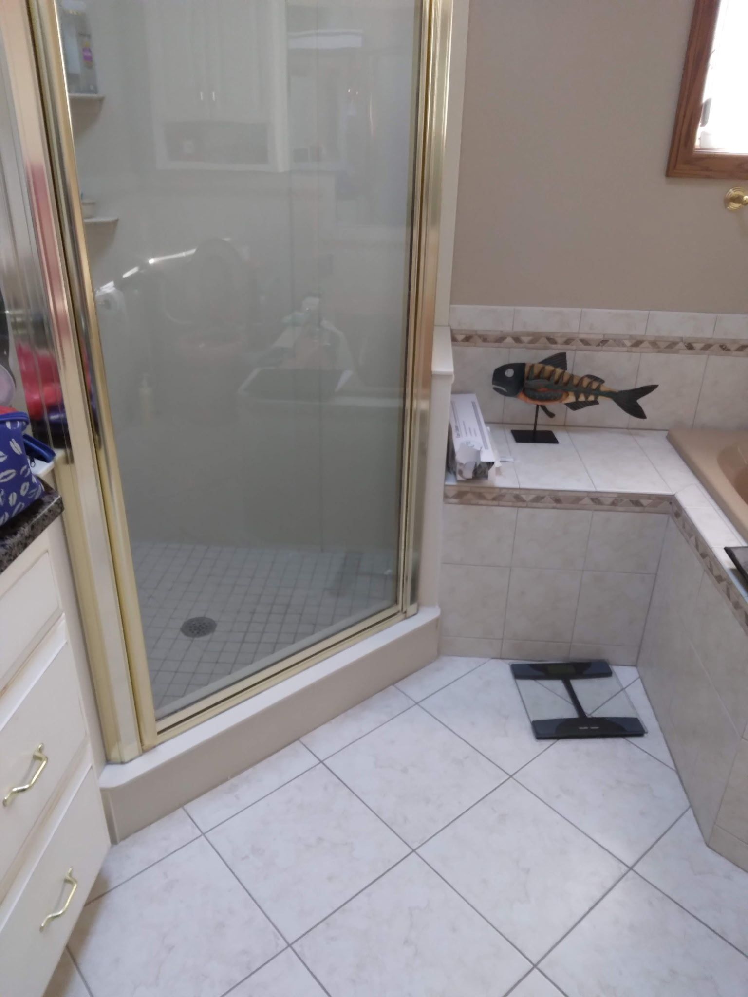 Bathroom with a gold-framed shower, tiled floor, and a built-in tub with decorative fish sculpture.