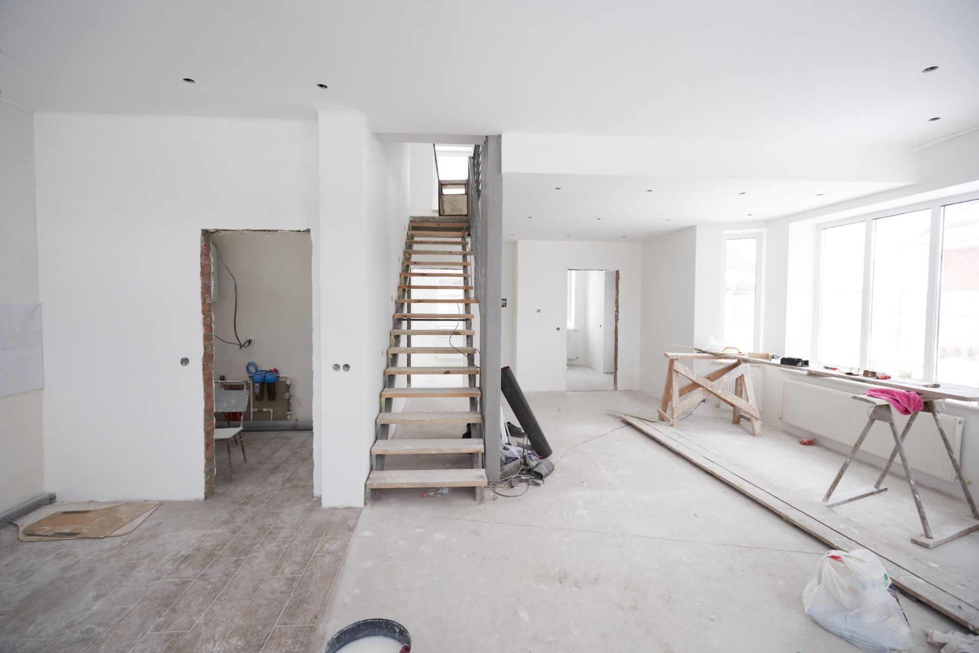Interior during renovation, featuring a wooden staircase, unfinished walls, and construction materials.
