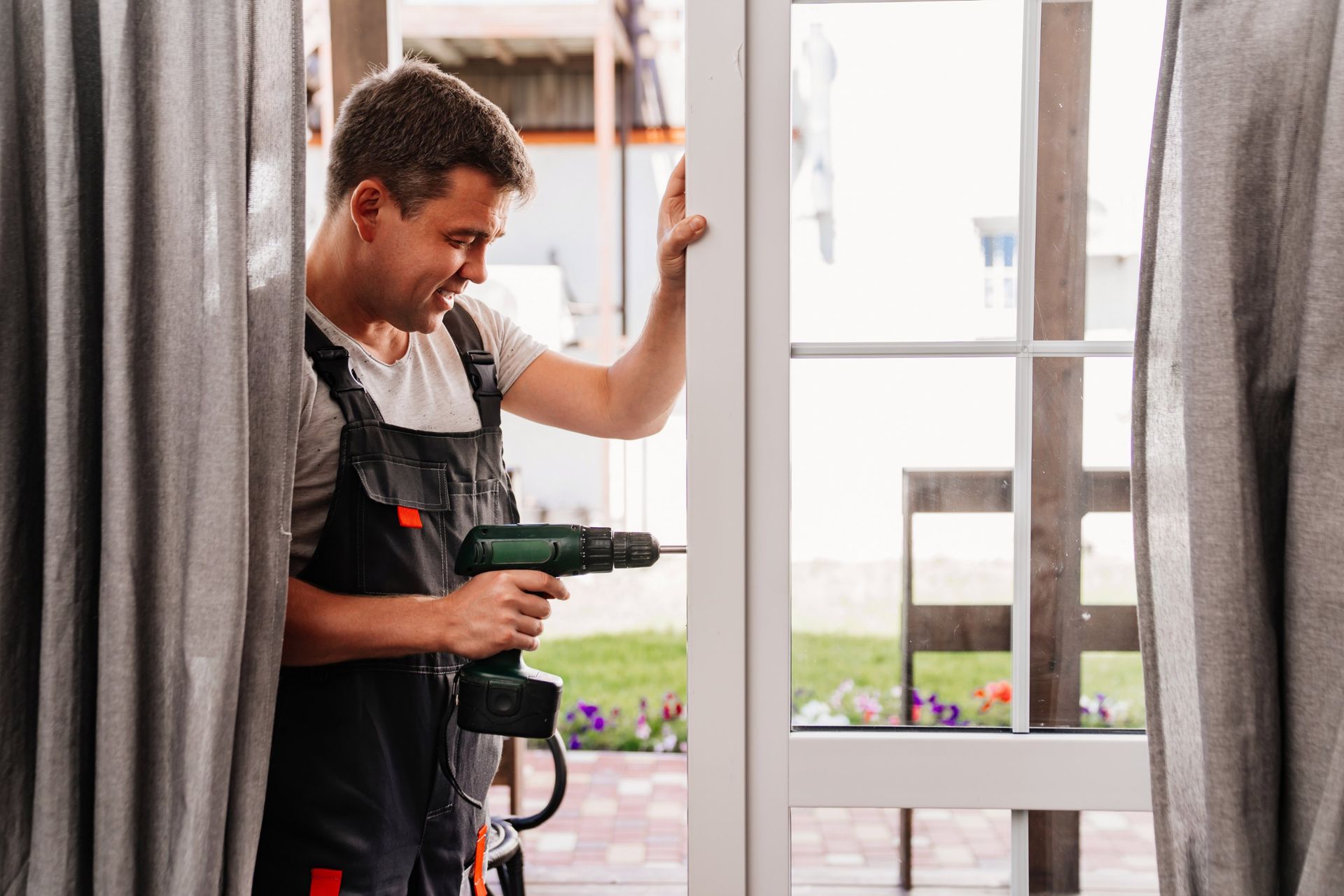 Man using a drill on a white door frame. He is in overalls and appears to be working indoors.