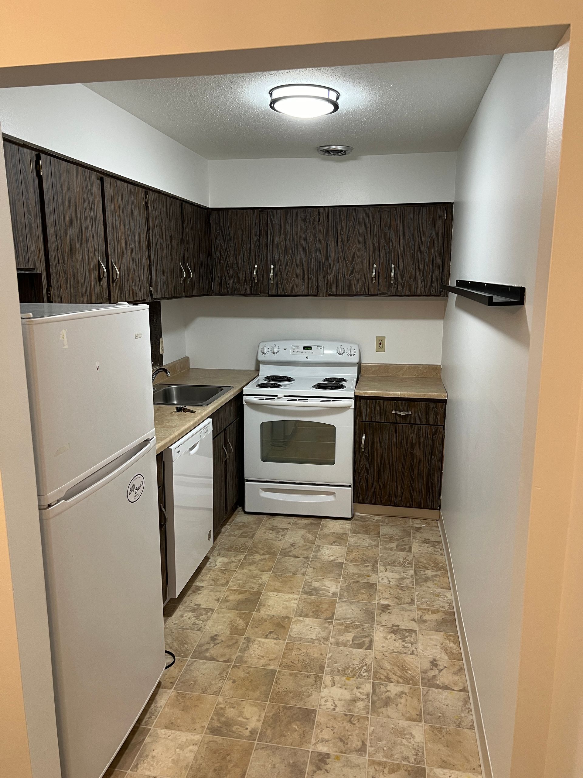 Kitchen with white appliances, dark cabinets, and patterned flooring.
