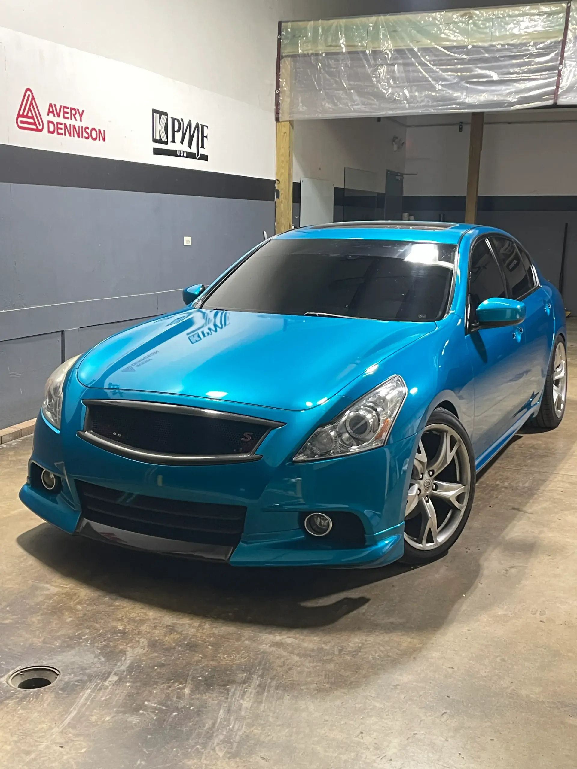 Black Corvette in a garage with hexagon-shaped lights. Garage has advertising posters hanging on the wall.