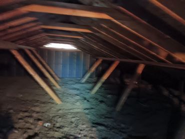 Interior of an attic with wooden beams, insulation, and a small window.