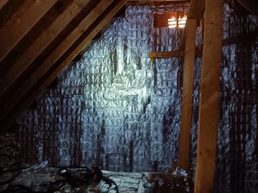Attic with wood beams and silver reflective insulation. A light shines on the insulation.