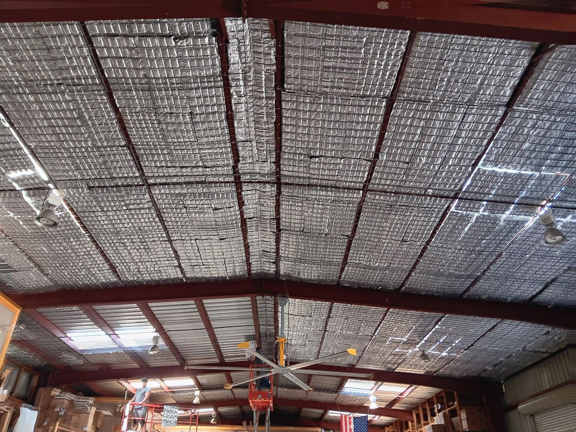 Ceiling of a warehouse with silver insulation panels attached to the metal beams.