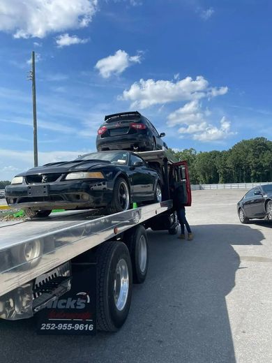 Black cars on a tow truck. Man standing. Sunny day.