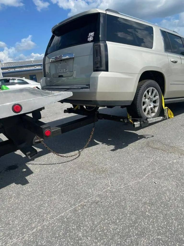 Silver SUV being towed on a flatbed tow truck, outdoors on pavement under a blue sky.
