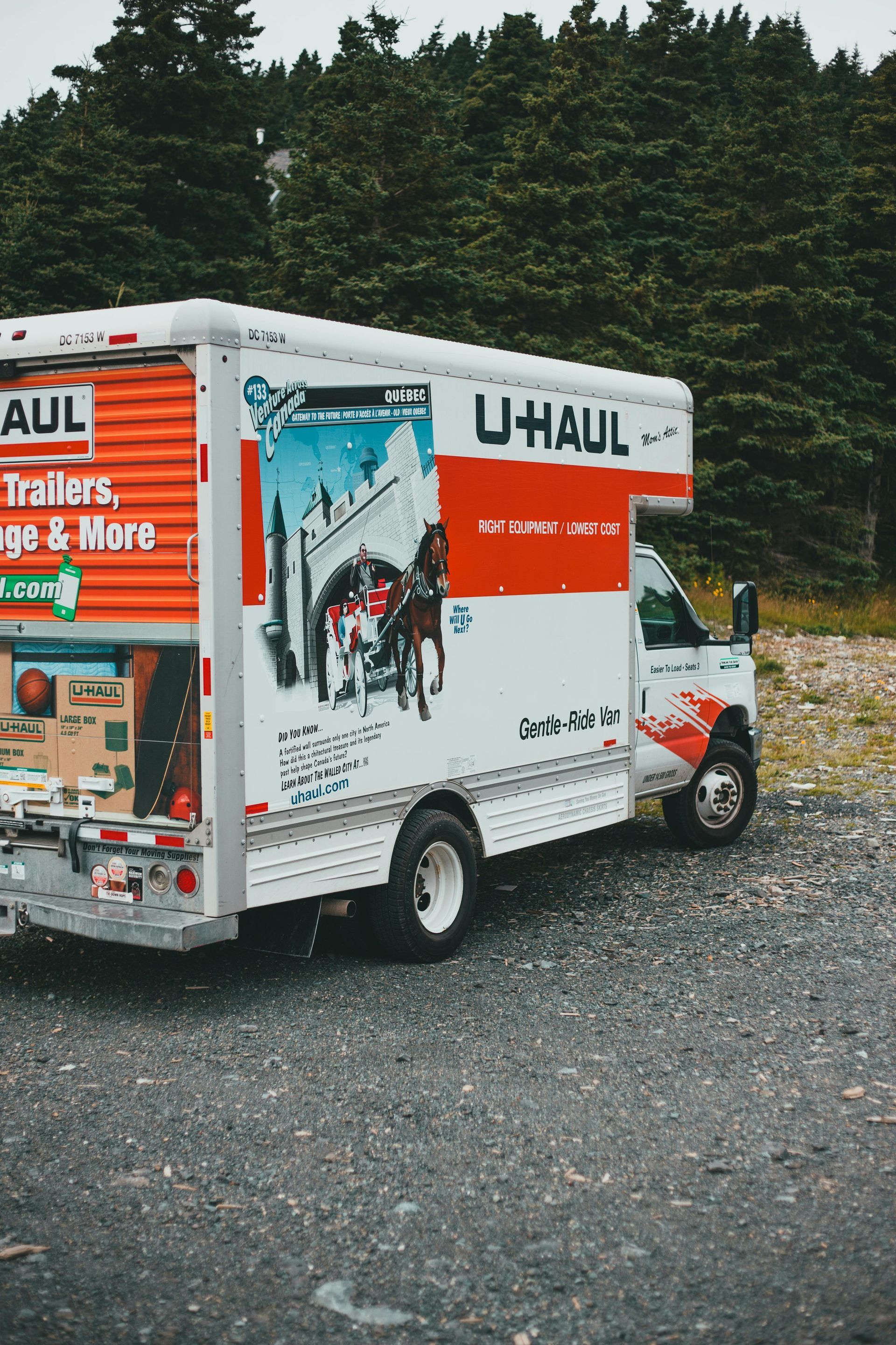 U-Haul truck parked on gravel with trees in the background; side panel has artwork.