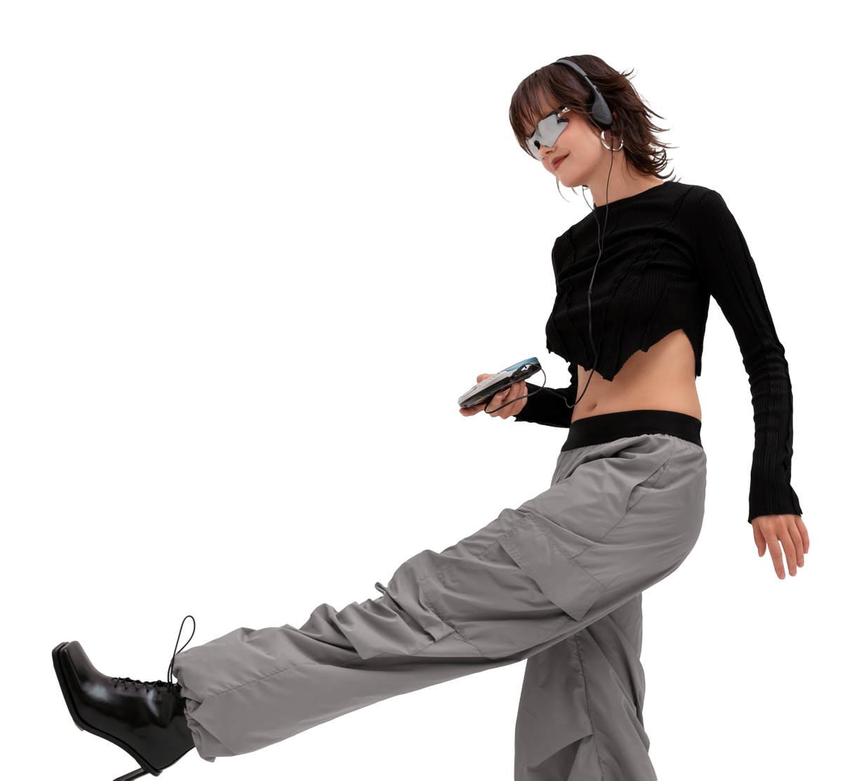 Mujer escuchando música, dando un paso al frente. Pantalones grises, camiseta negra y gafas de sol.