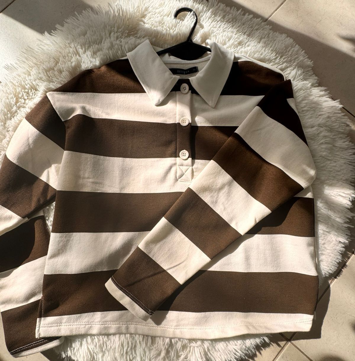 Camisa con cuello a rayas marrones y blancas en una percha