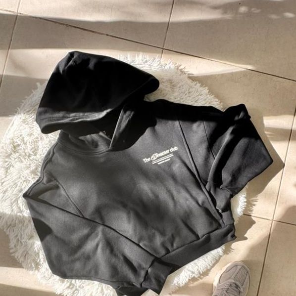Sudadera con capucha negra con texto blanco sobre una alfombra blanca